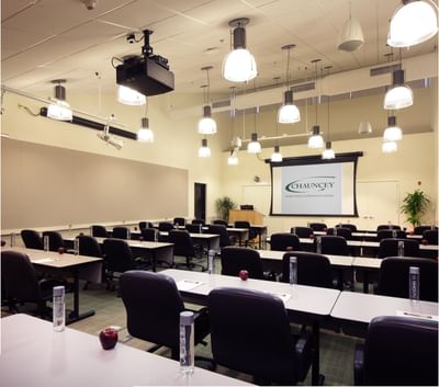 Conference room with rows of tables, chairs, pendant lighting, and projection screen at Aramark Chauncey Conference Center