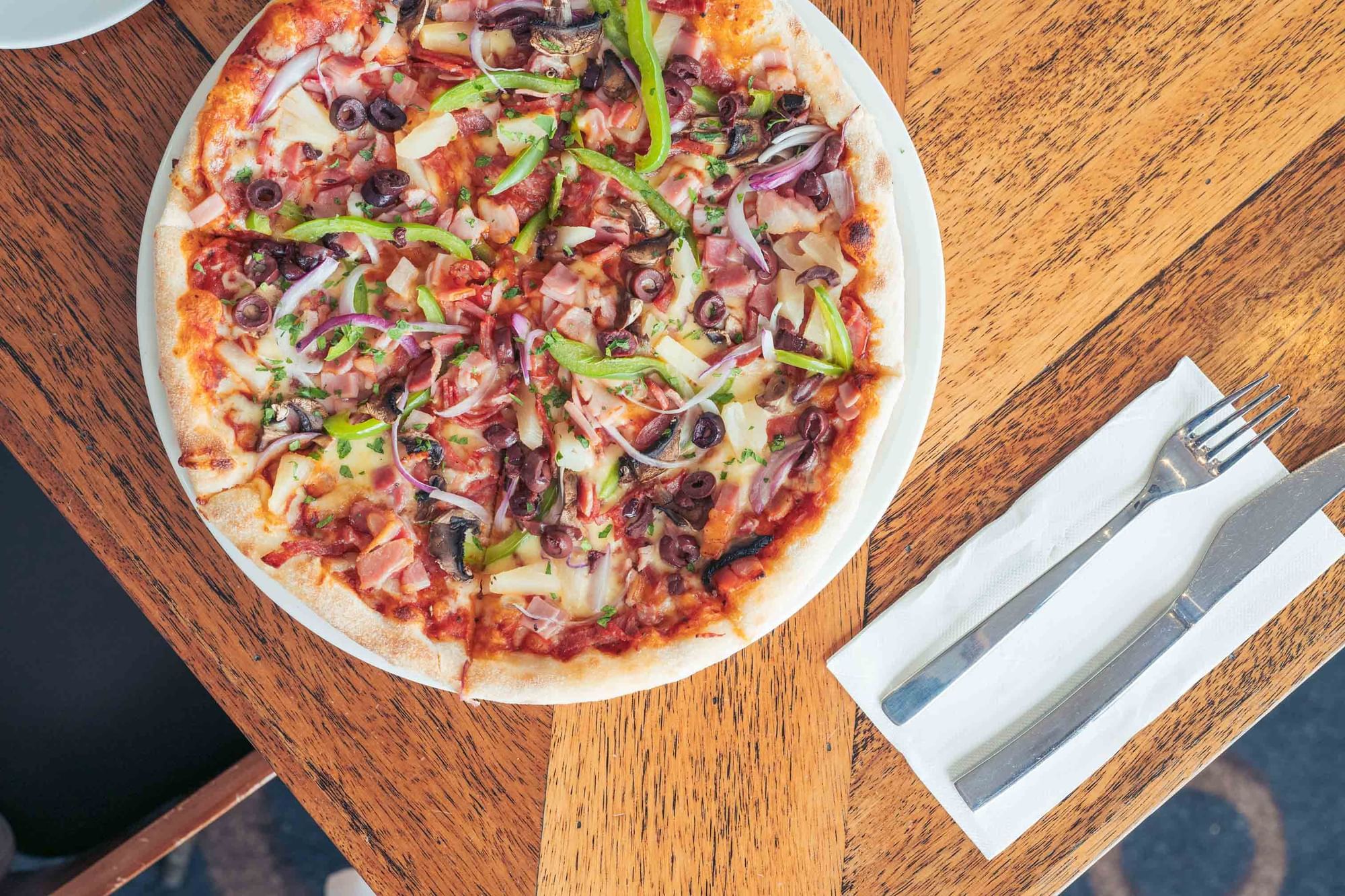 A whole pizza on a plate with a fork and knife on a paper napkin next to it.