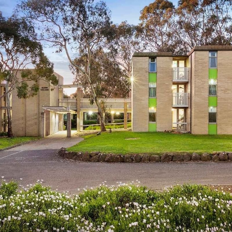 Modern building with green accents and white flowers in front at La Trobe University - Glenn College.