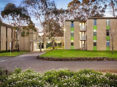Modern building with green accents and white flowers in front at La Trobe University - Glenn College.