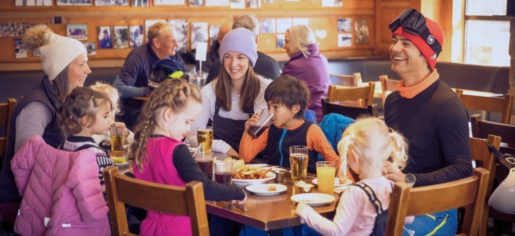 Families enjoying après-ski dining at a cozy Whistler restaurant, with children and parents sharing food and drinks together.