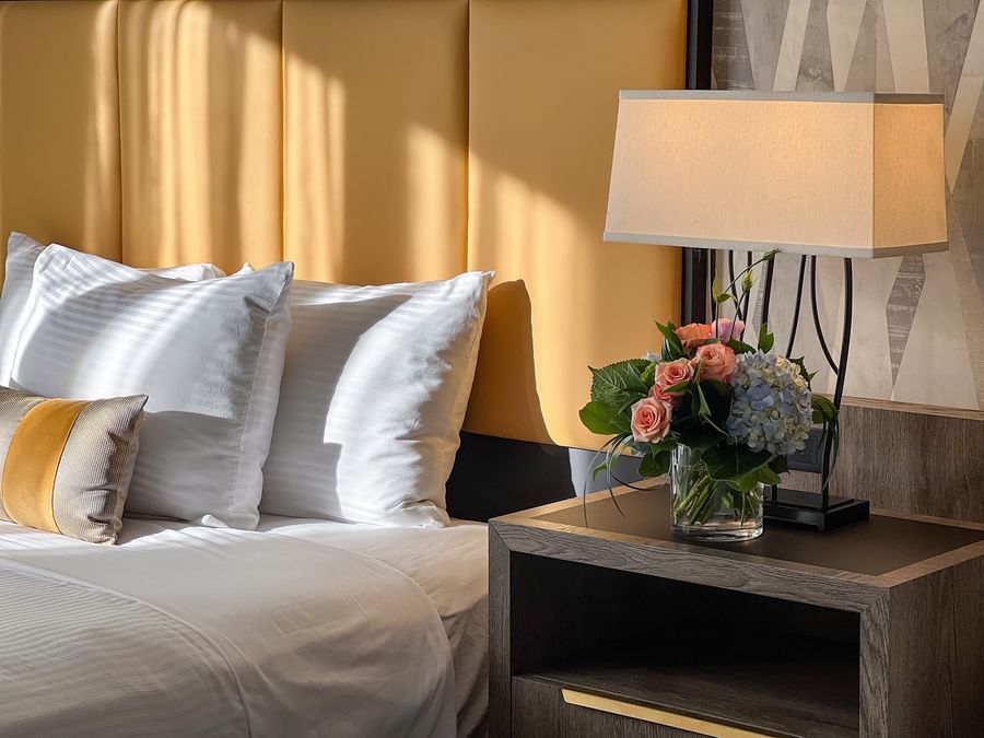Elegant hotel bedroom with a white bed, yellow accent pillow, flowers, and a nightstand at Warwick Seattle.