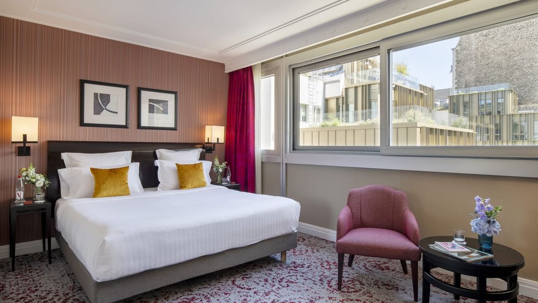  Deluxe Room features king bed by a pink armchair and round table under a large window at Warwick Paris Champs Elysées