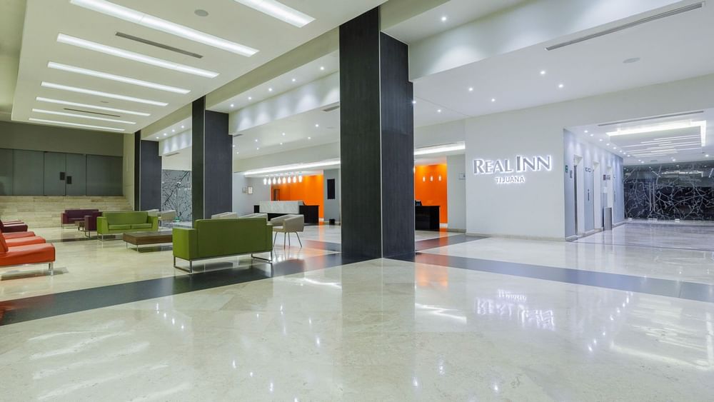 Lobby with sofas by pillars under a bright ceiling, surrounding a glossy marble walkway at Real Inn Tijuana
