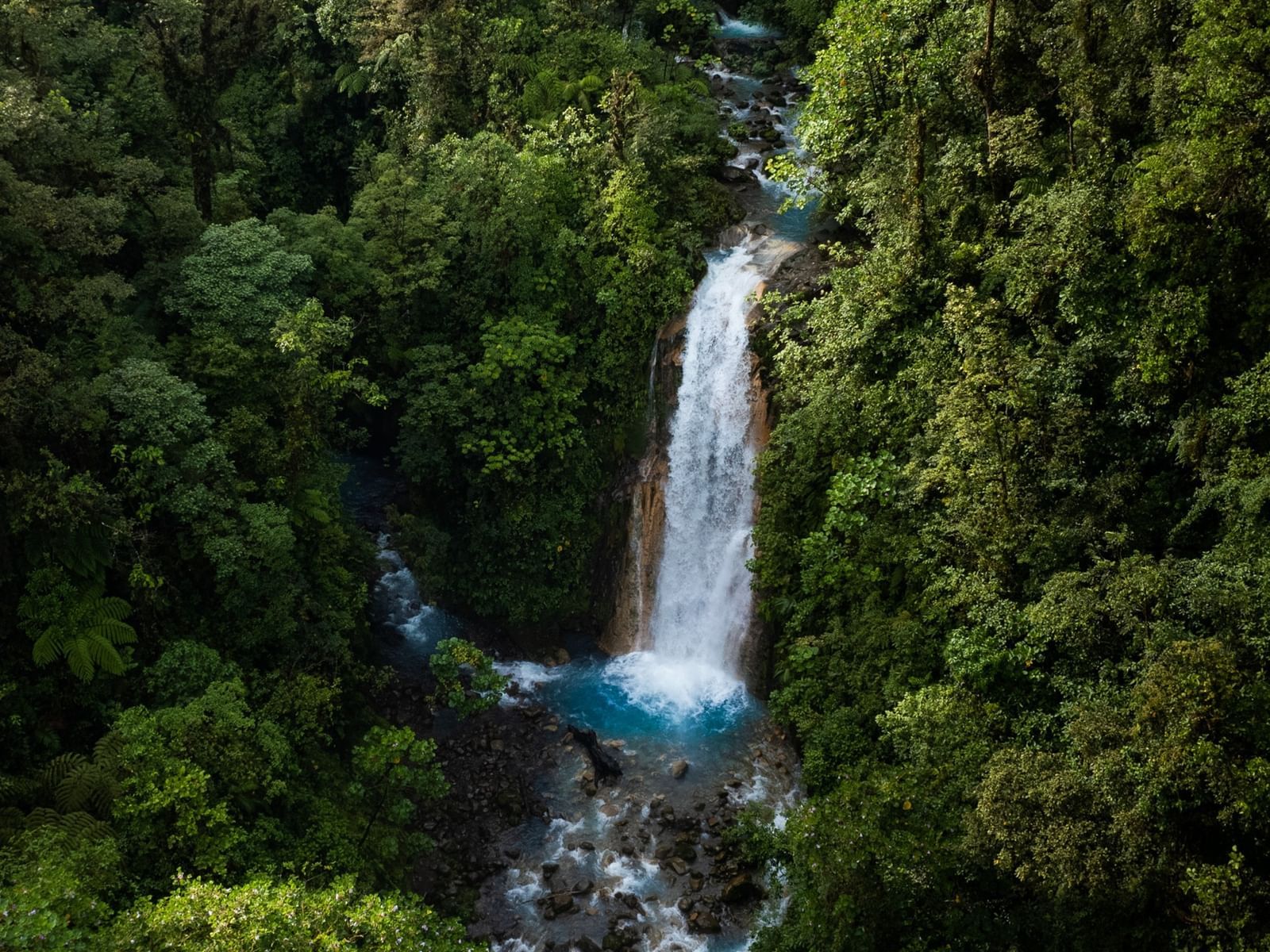 Aerial view of Rio Celeste waterfall amid lush green forest near El Silencio Lodge and Spa