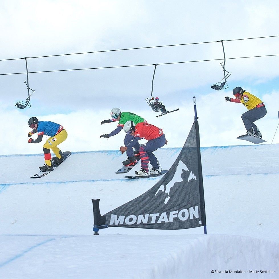 Snowboarders performing tricks in a competition with Montafon banner.