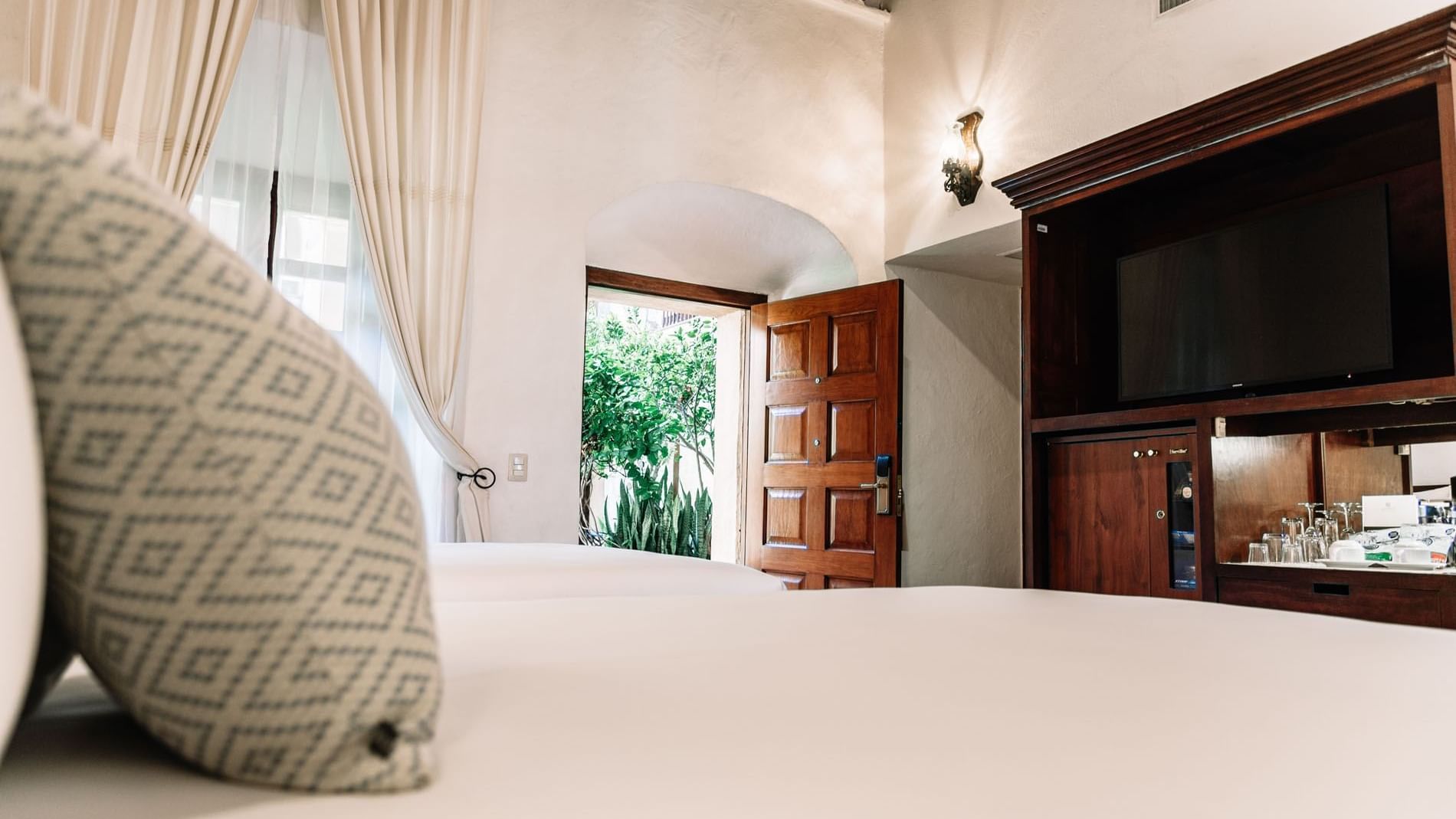 Elegant wooden furniture with glassware and a TV by the bed in 2 Double Superior Suite at Quinta Real Oaxaca