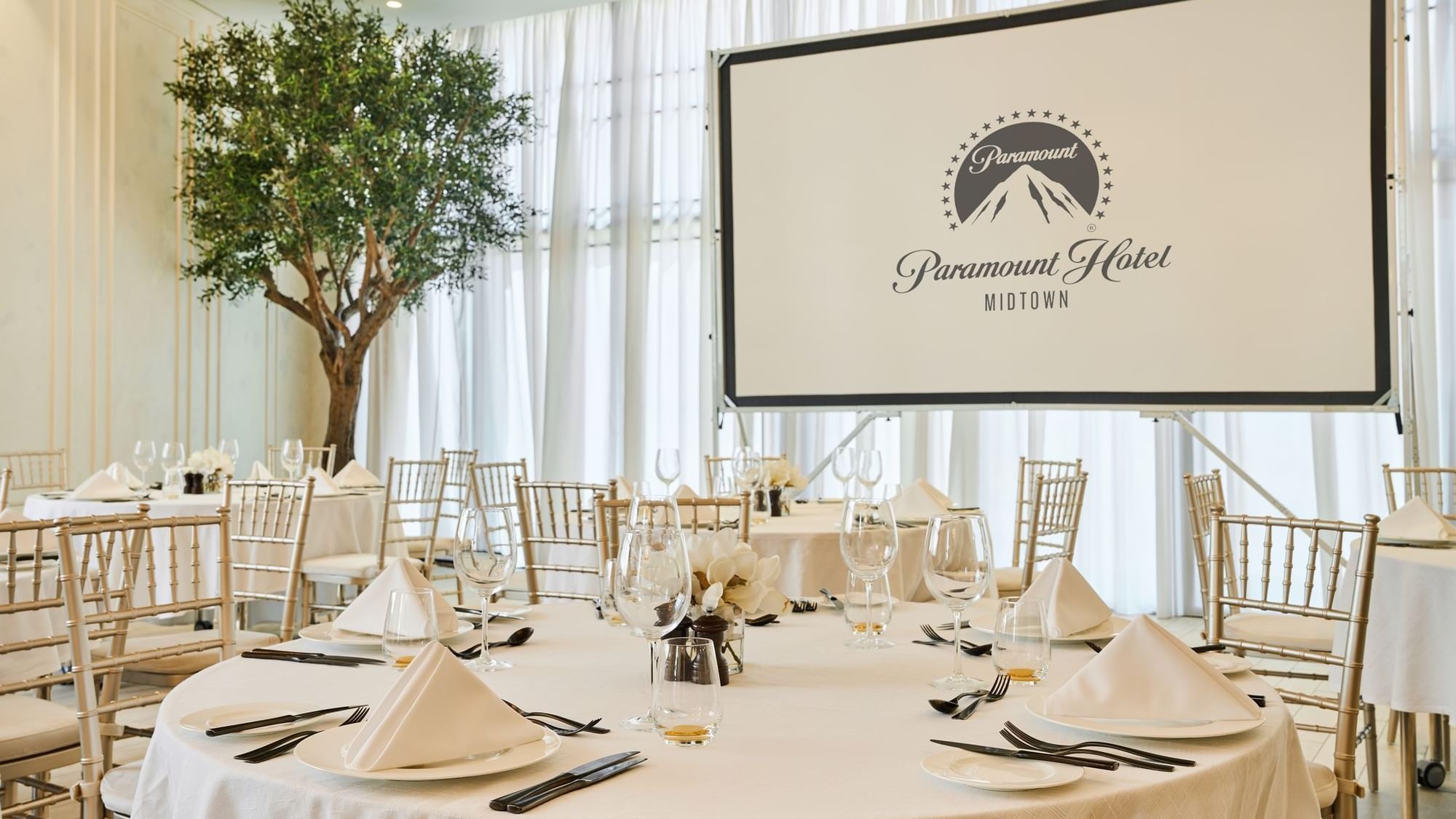 Tables with place settings ready for an event at Paparazzi restaurant venue, Paramount Hotel Midtown, with projector screen