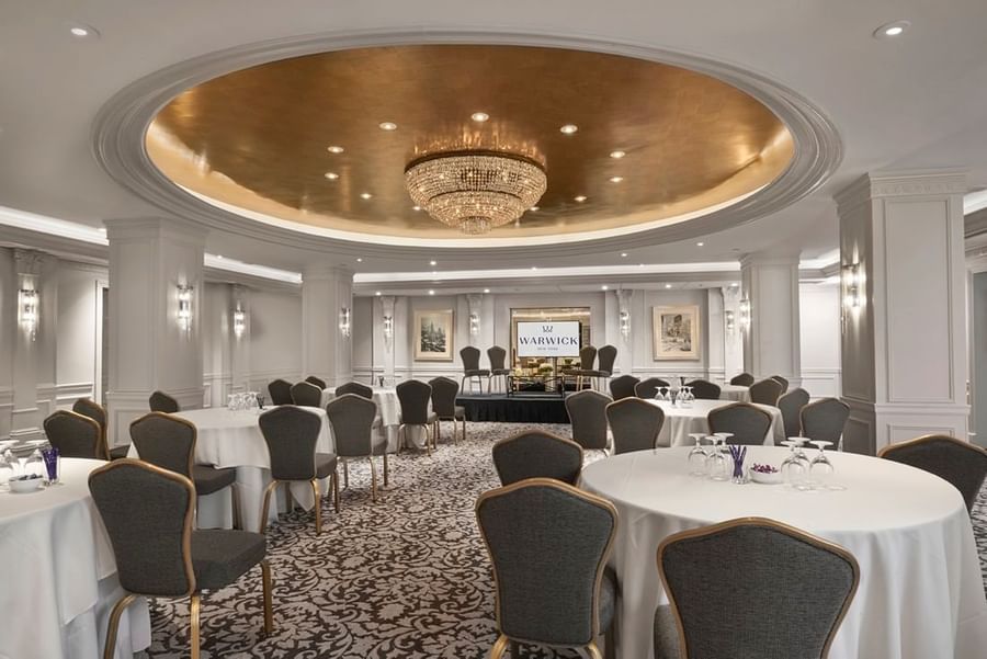 Grand ballroom with round banquet tables& chairs under a stunning gold dome and chandelier at Warwick New York