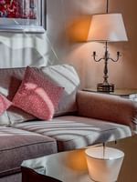 Grey sofa with red pillows by a mirrored side table under a lamp in Deluxe Suite Accessible at Warwick Melrose Dallas