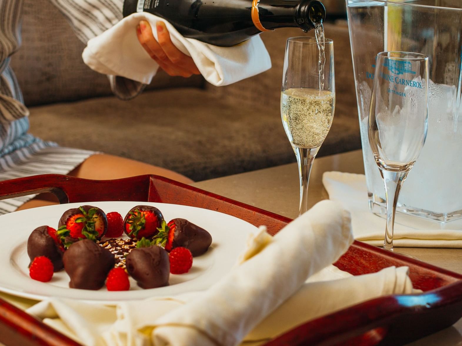 Woman pouring champagne in flutes next to a plate of chocolate covered strawberries