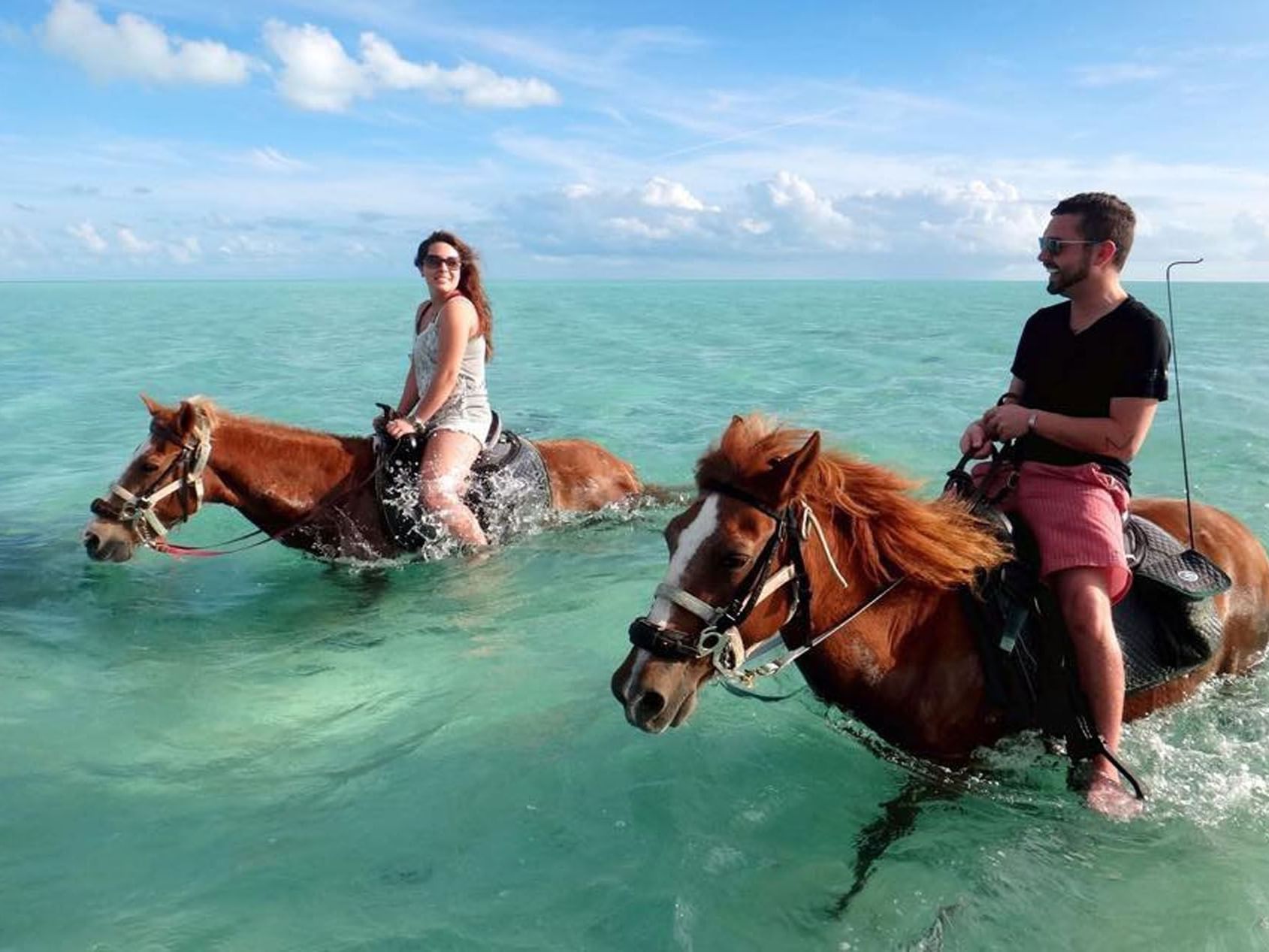 Two riders enjoy horseback riding in shallow turquoise waters near Windsong Resort On The Reef