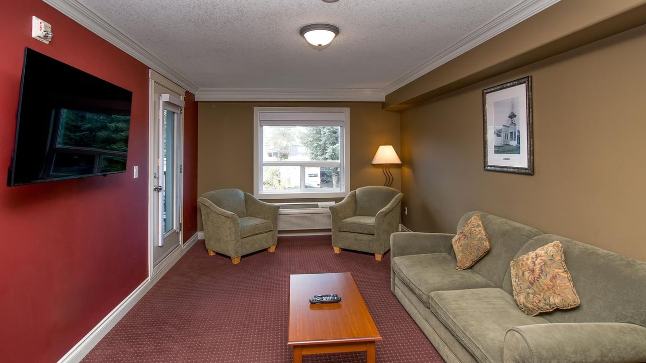 Cozy hotel lounge with sage green sofa, armchairs, coffee table, and wall-mounted TV at Coast Edson Hotel.