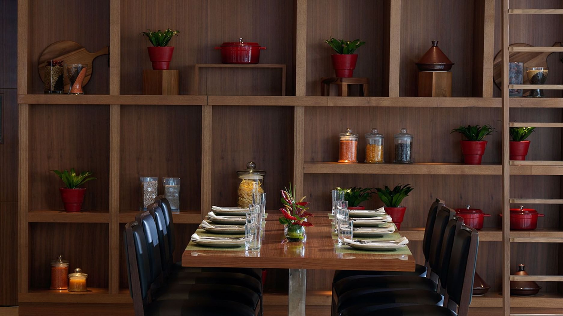 Maison Cafe Damac Maison dining area with table set for six, shelving with jars, and dark chairs at DAMAC Maison Cour Jardin
