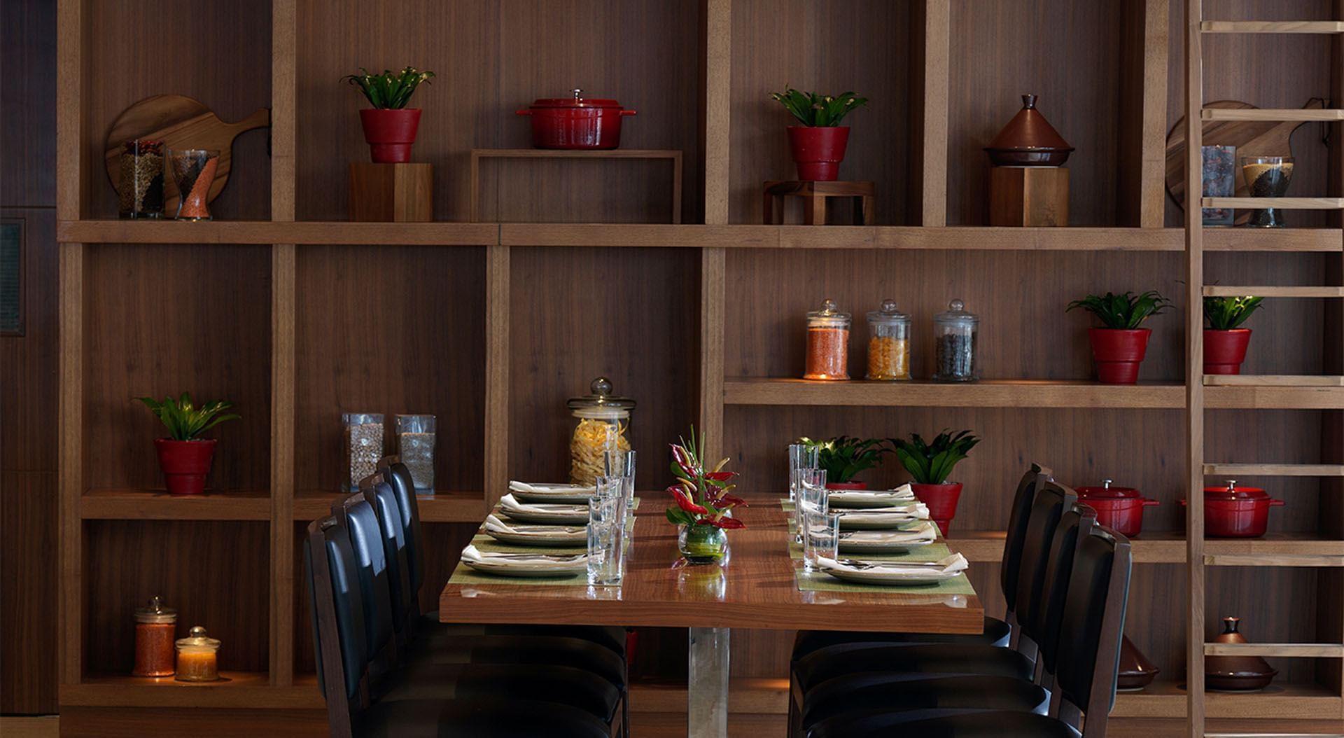 Maison Cafe Damac Maison dining area with table set for six, shelving with jars, and dark chairs at DAMAC Maison Cour Jardin
