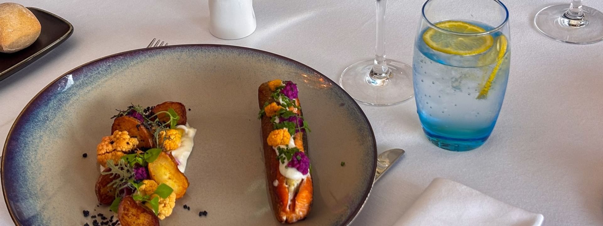 Seared salmon and roasted vegetables with a glass of wine on a white table in Téséo at Warwick Geneva
