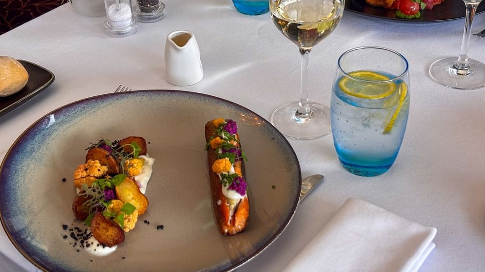 Seared salmon and roasted vegetables with a glass of wine on a white table in Téséo at Warwick Geneva