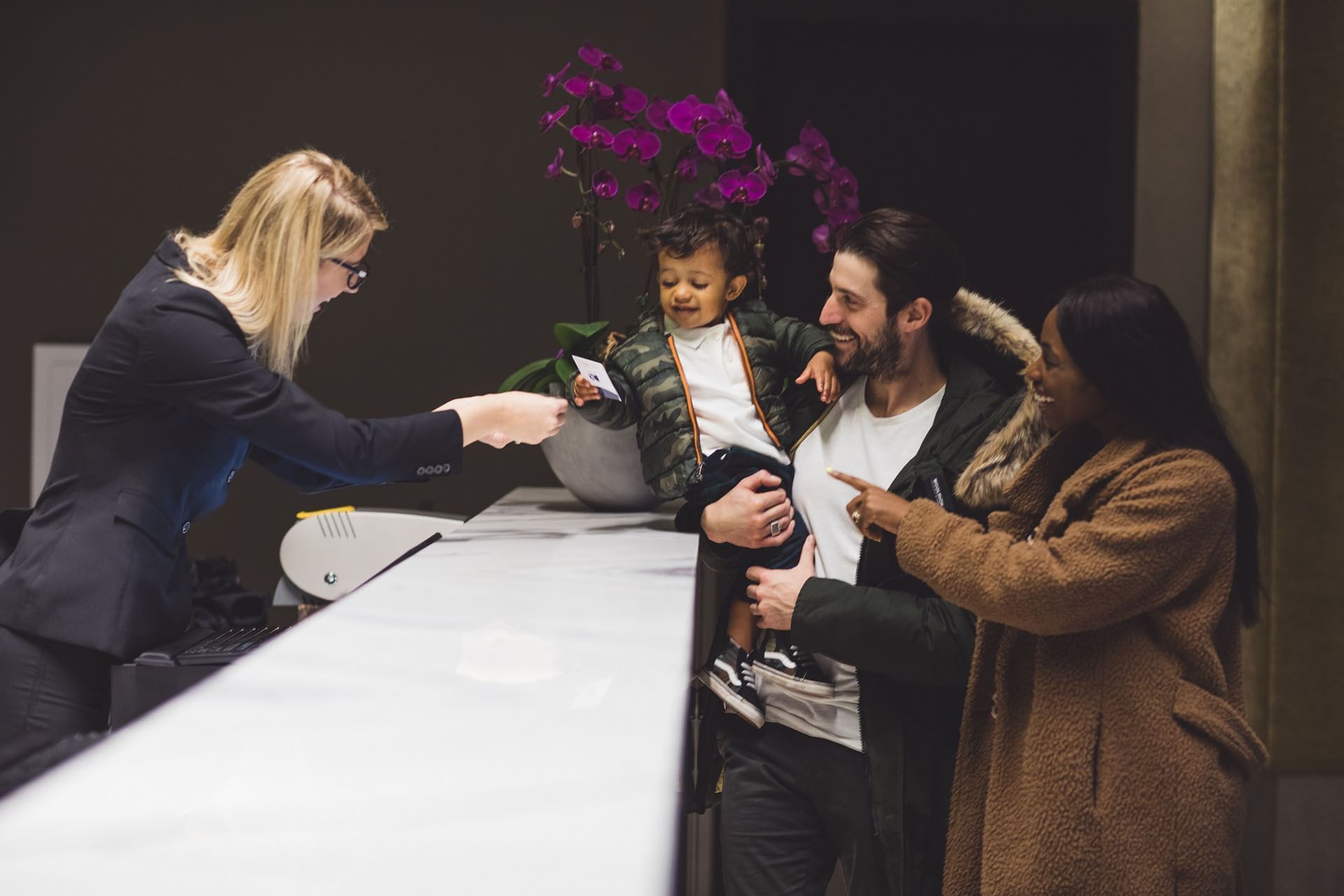 Receptionist welcoming family with young child across sleek front desk counter at Hotel X Toronto