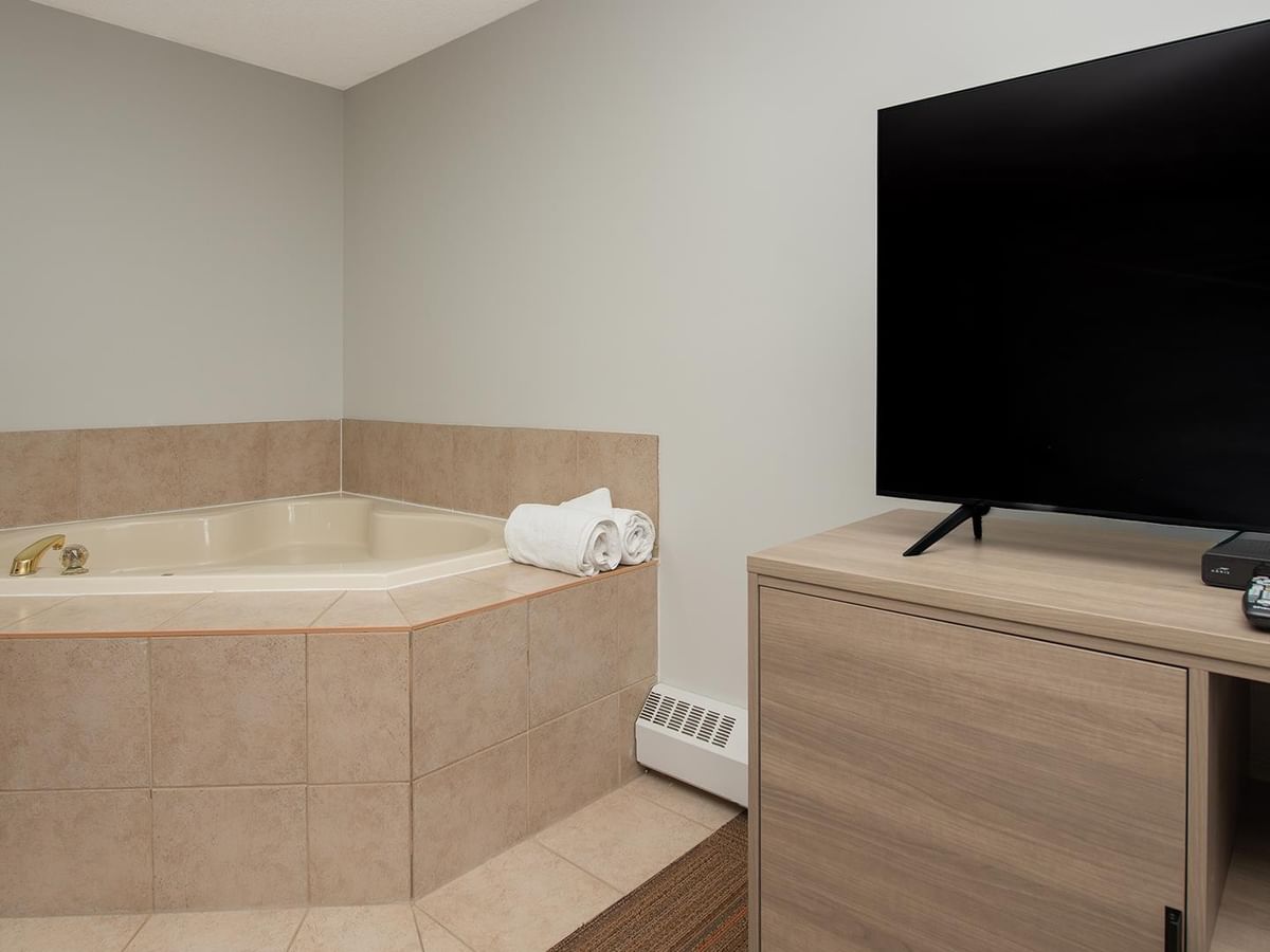 Coast Premium King Suite with beige-tiled soaker tub, flat-screen TV, and modern furnishings.