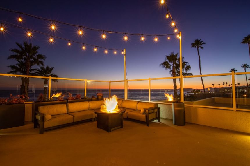 Fire pit and couch at sunset with string lights and palm trees