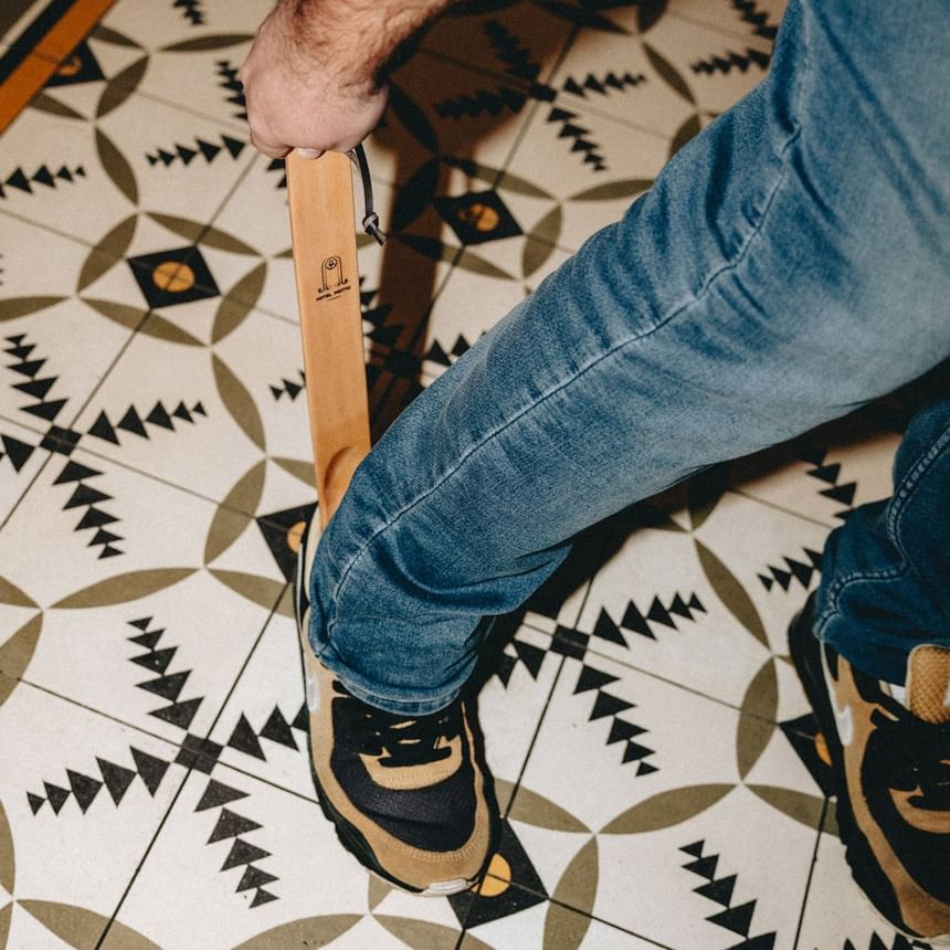 Mann mit Holzschuh-Schuhlöffel von Hotel Motto Wien auf gemustertem Boden stehend bei Hotel Motto