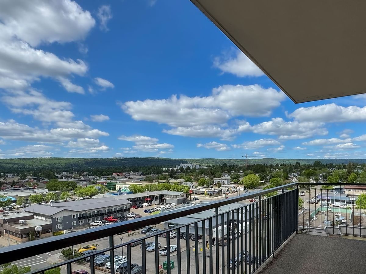 Balcony with metal railings overlooking a cityscape with buildings, trees, and a parking lot.