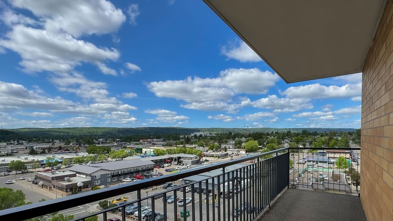 Balcony with metal railings overlooking a cityscape with buildings, trees, and a parking lot.