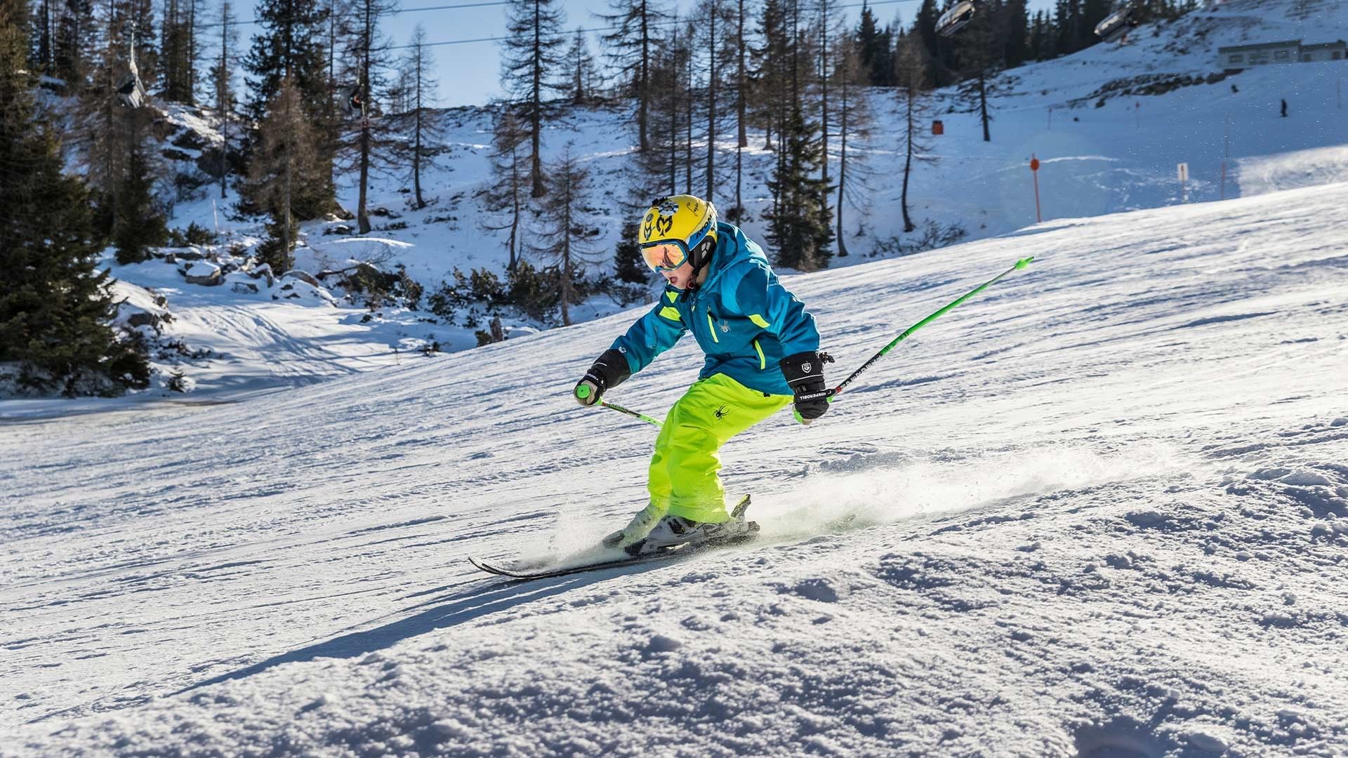 Skier in blue jacket and yellow helmet navigating a snowy slope with green ski poles.