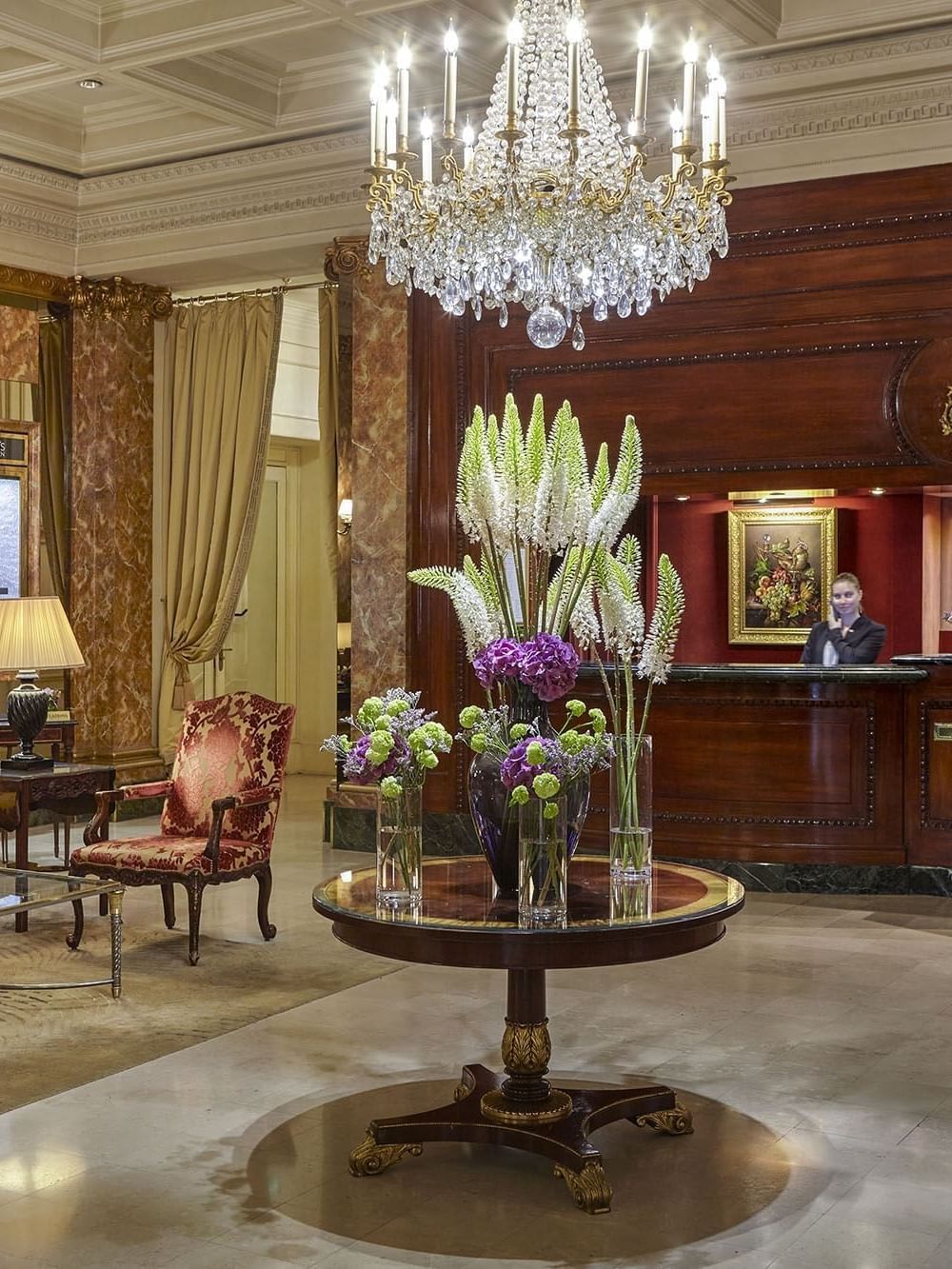 Hotel Westminster Paris lobby with a crystal chandelier placed over a round table featuring floral arrangements by a desk