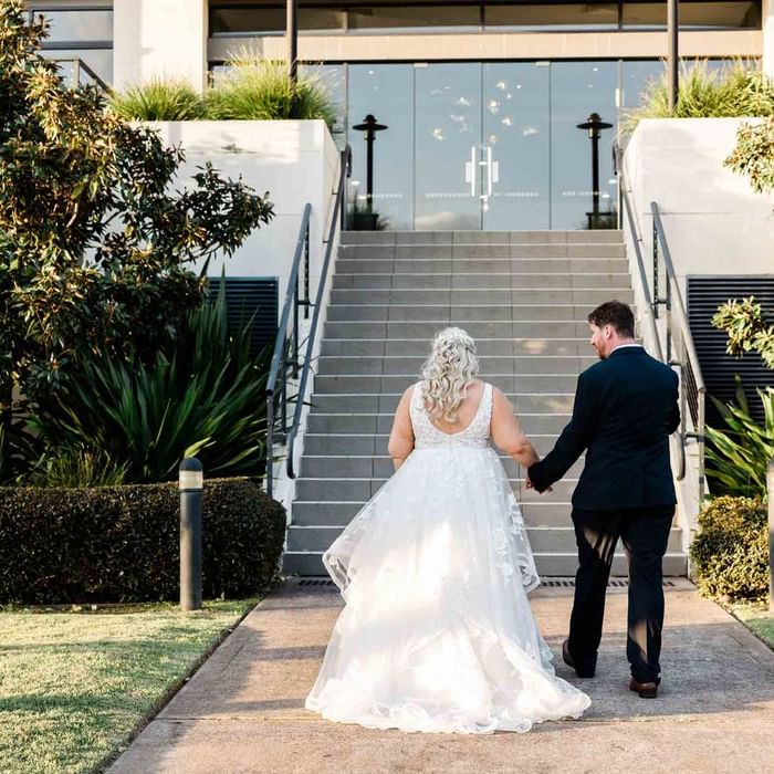 Bride holding hands with groom walking upstairs at Mercure Kooindah Waters