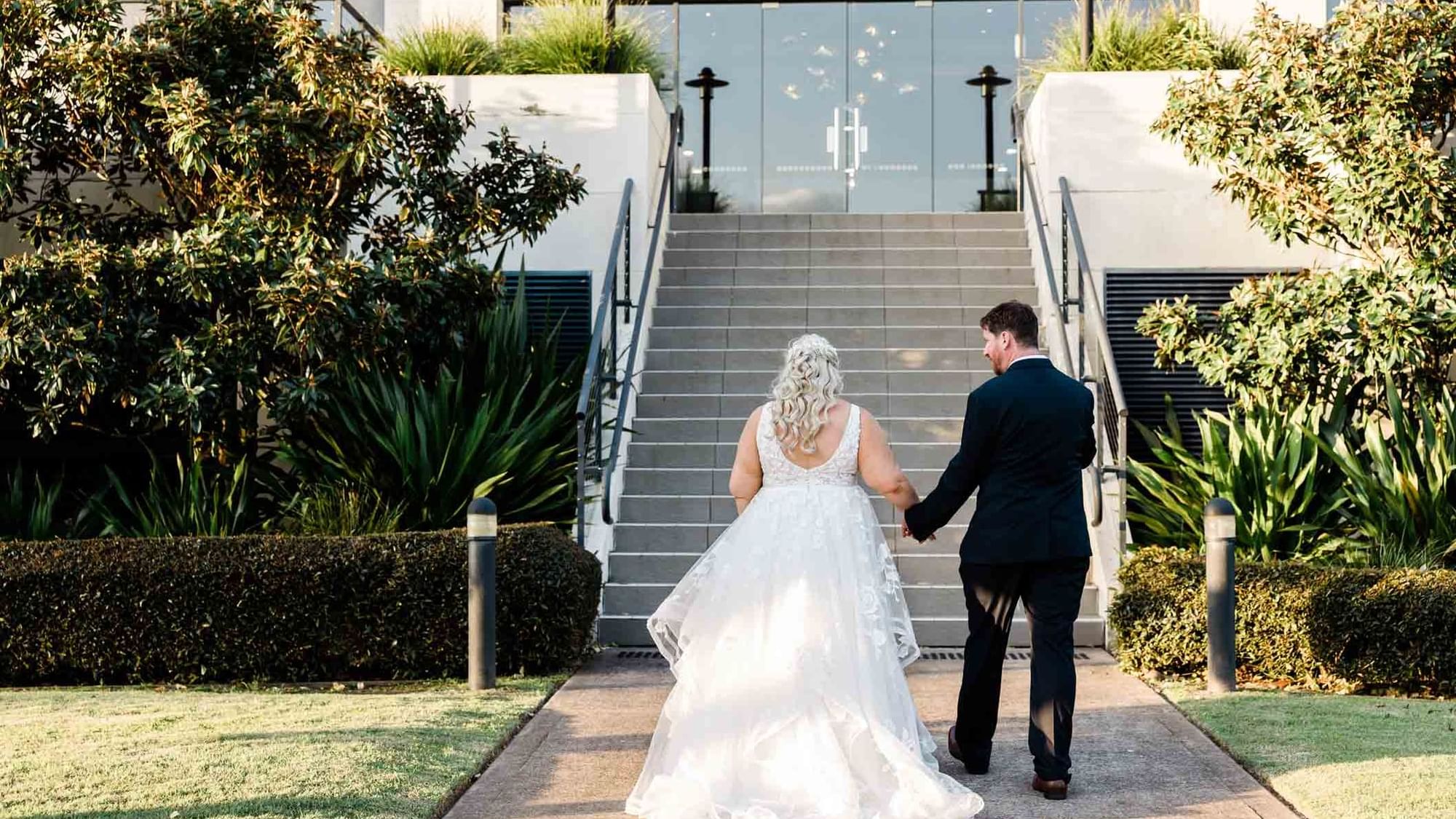 Bride holding hands with groom walking upstairs at Mercure Kooindah Waters