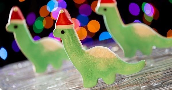 Three green dinosaur cookies, each topped with a festive Santa hat as part of the menu at Jollywood Nights 