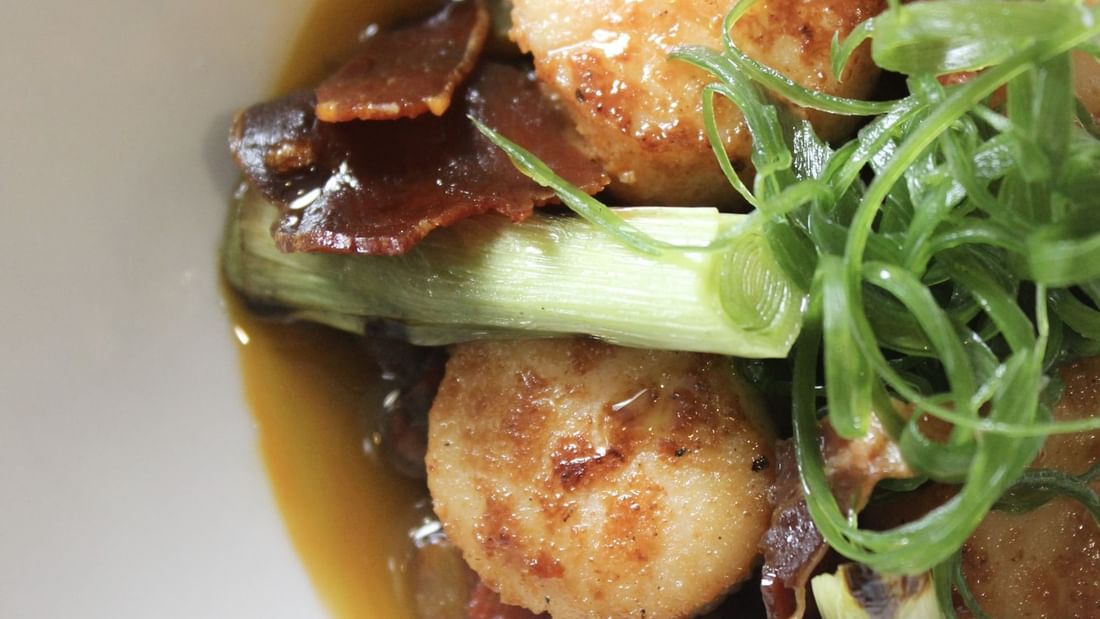 Bowl filled with scallops, bacon, and greens showcasing Karinya’s Refreshed Menu.