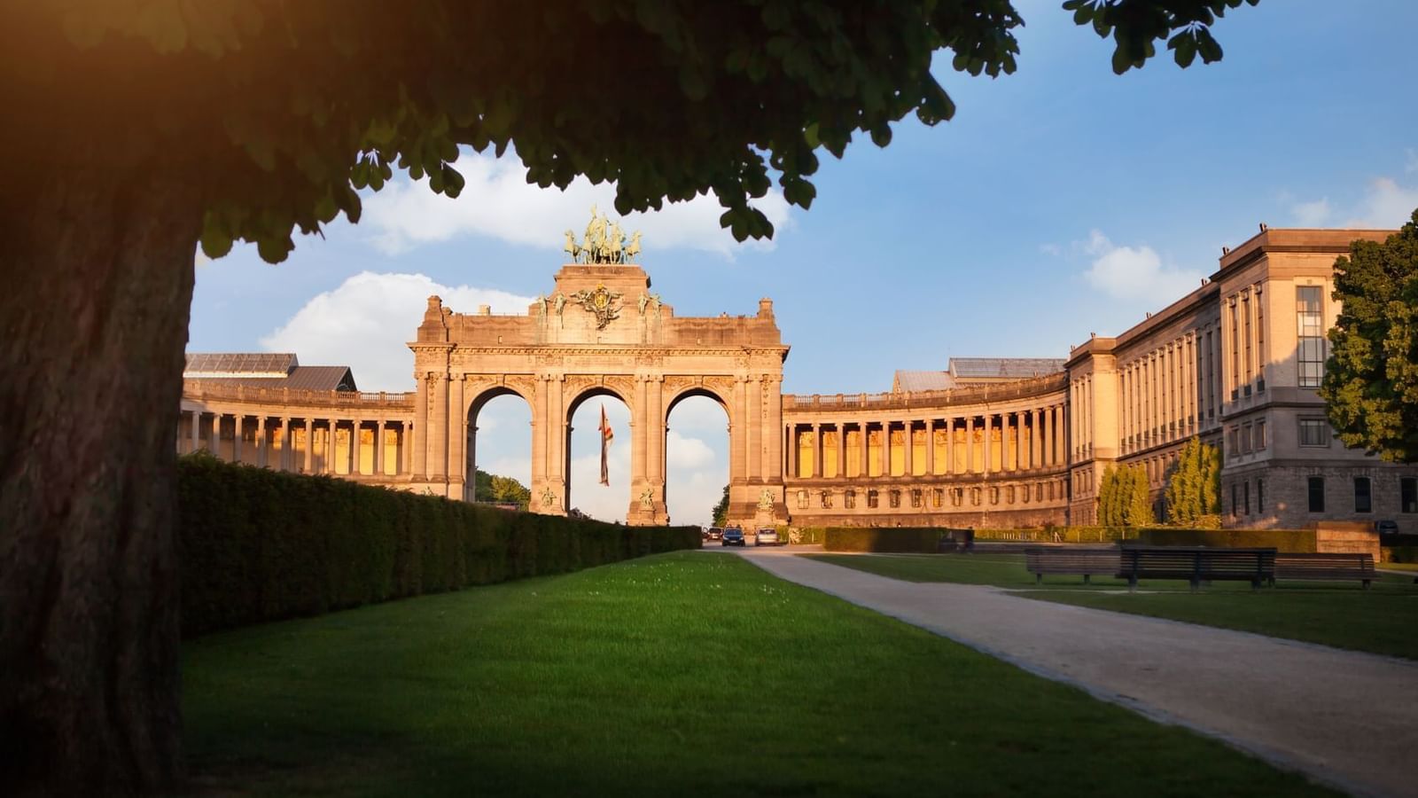 Historic stone archway monument at Cinquentenaire park with lush greenery near Warwick Grand Place Brussels