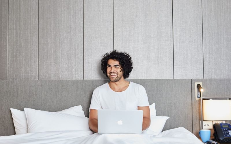 A man working on laptop in a bed at Melbourne Central Hotels