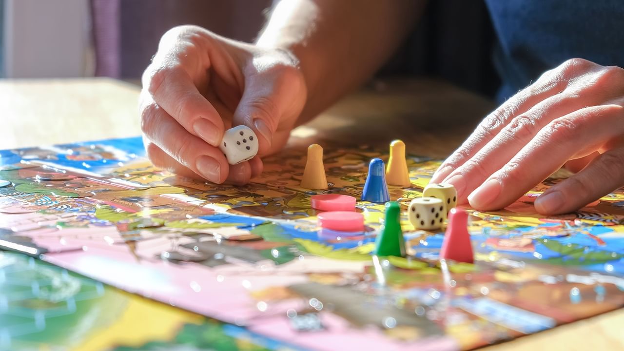 Two people playing a colorful board game with dice and game pieces