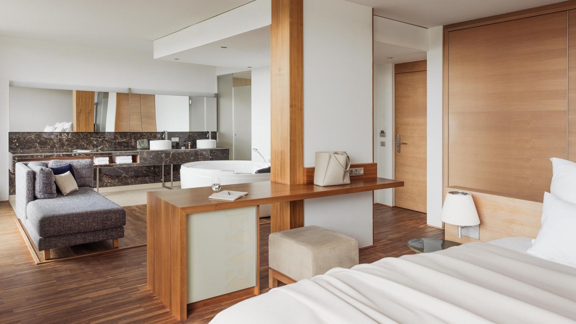 Elegantes Hotelzimmer mit großem Bett, Couch, Schreibtisch und modernem Badezimmer mit Wanne.