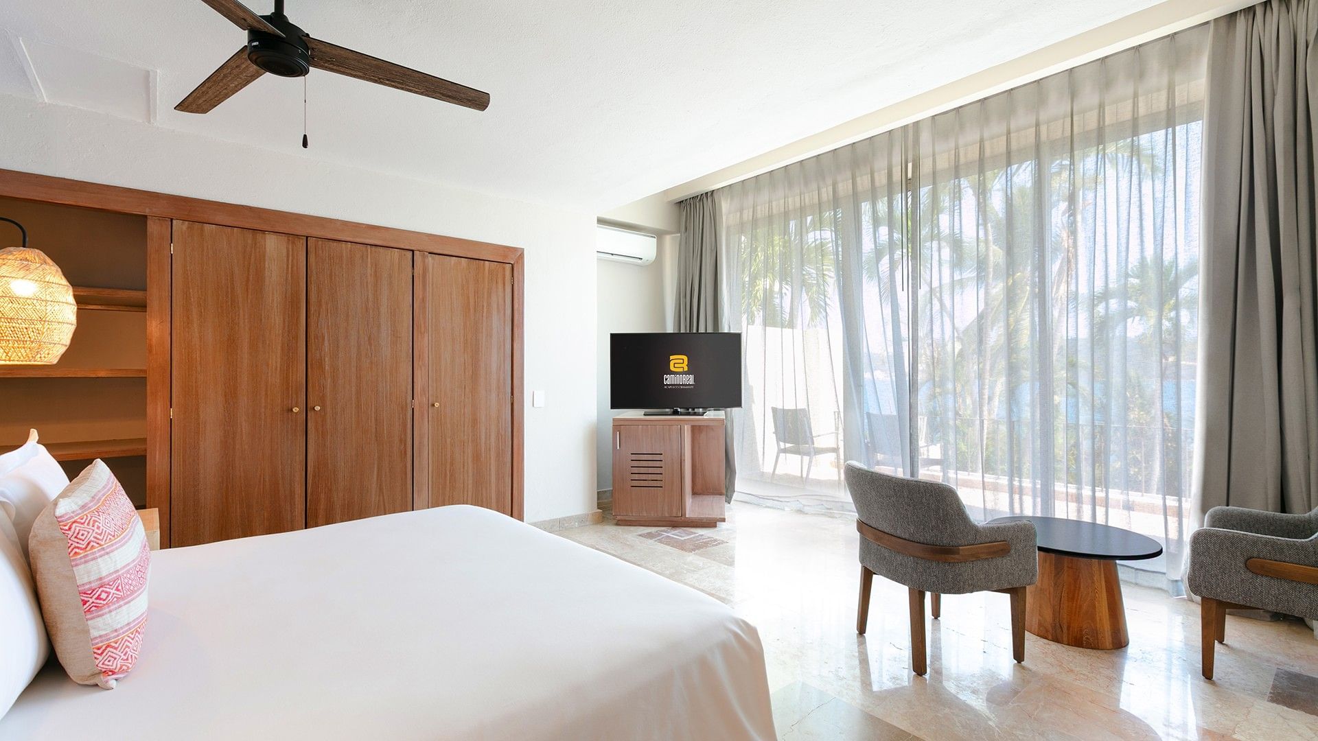 King Junior Suite with wooden wardrobes, a grey armchair, and a tropical palm view at Camino Real Acapulco Diamante