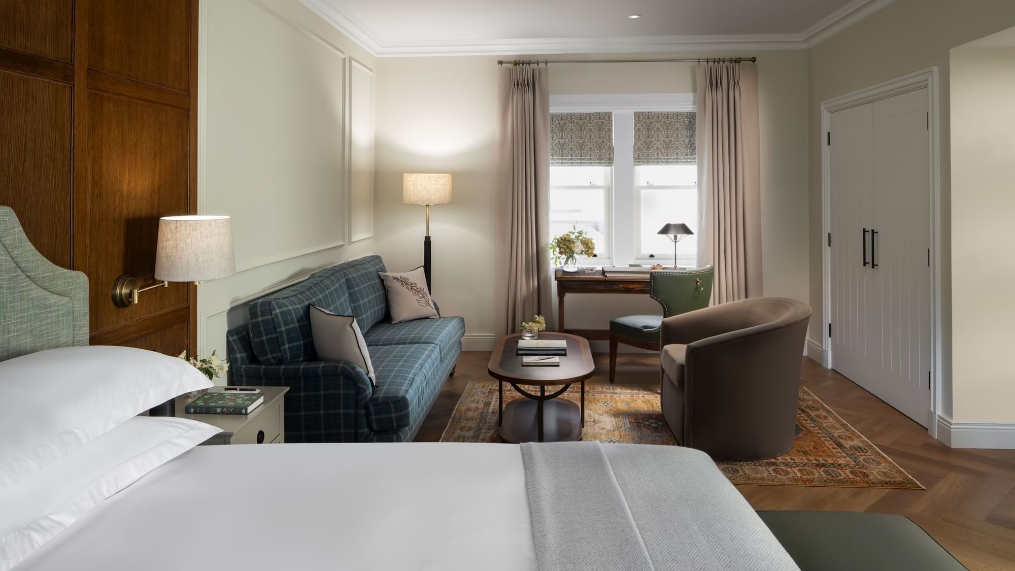 Bed with a lounge area featuring a plaid sofa, a work desk, by a large window in Garden Suite at Dunluce Lodge