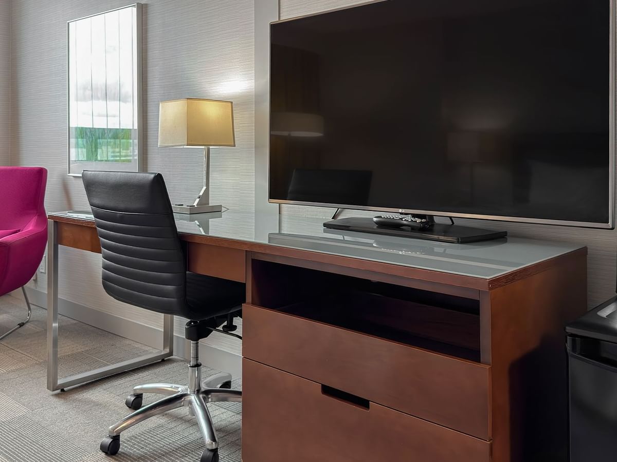Hotel room with flat-screen TV, work desk, chairs, coffee maker, and mugs.