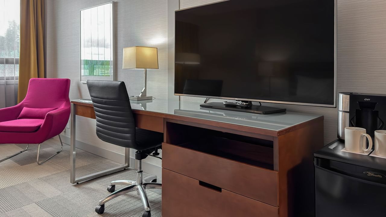 Hotel room with flat-screen TV, work desk, chairs, coffee maker, and mugs.