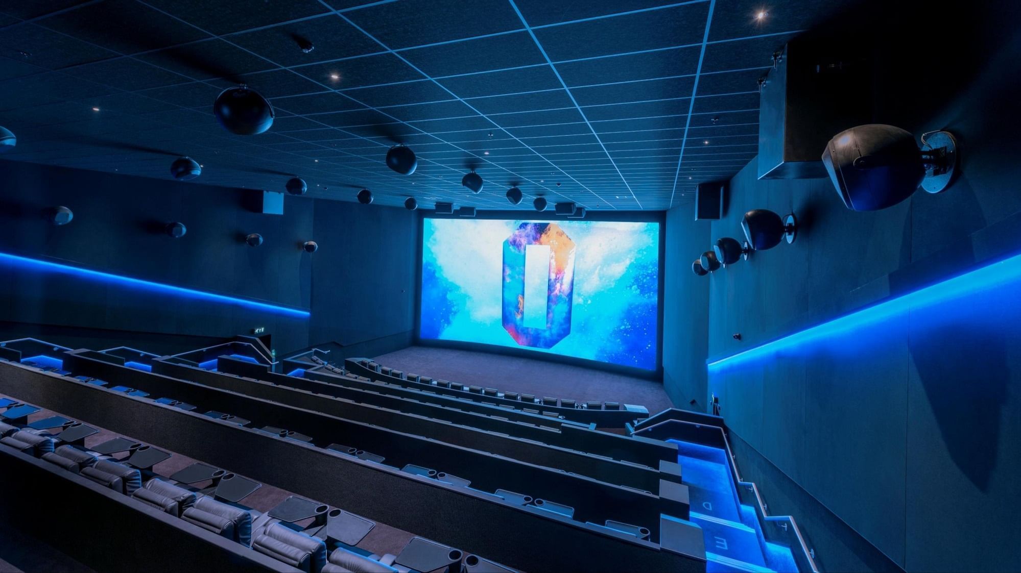 A spacious movie theater with a massive screen and blue lighting near The Londoner Hotel