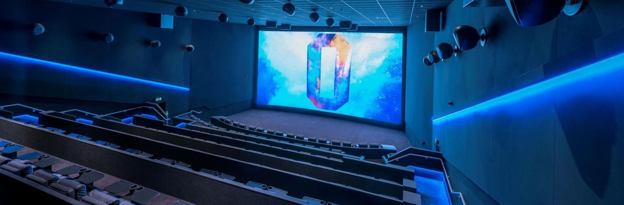 A spacious movie theater with a massive screen and blue lighting near The Londoner Hotel