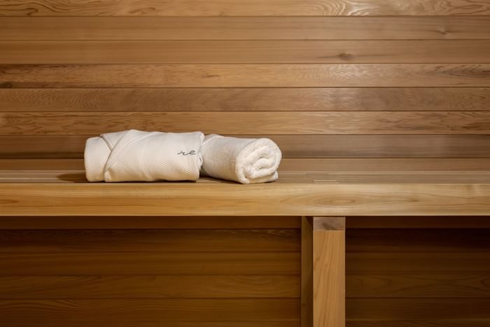 A white towel and a folded robe sit on a wooden bench in the sauna at ReStays Ottawa
