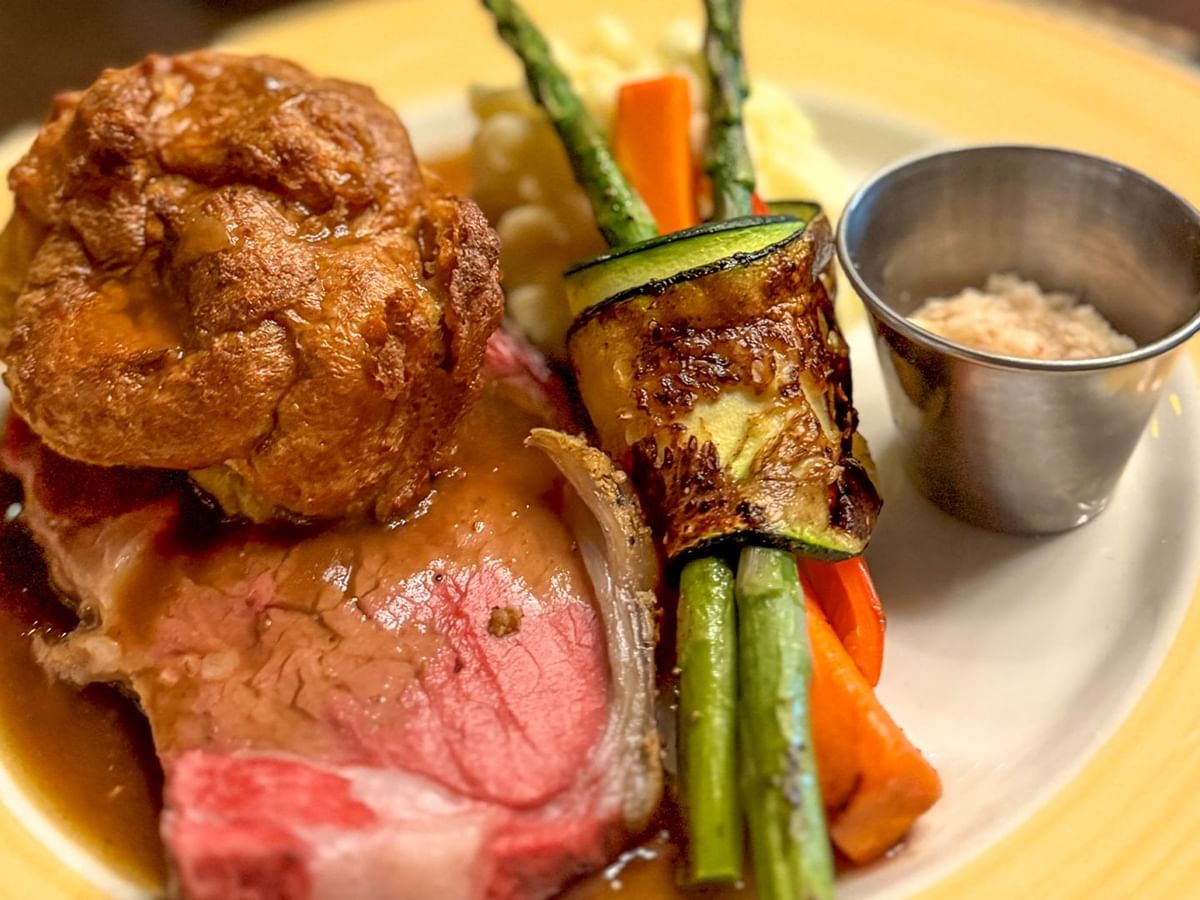Plate of beef, vegetables, and a cup of seasoning.