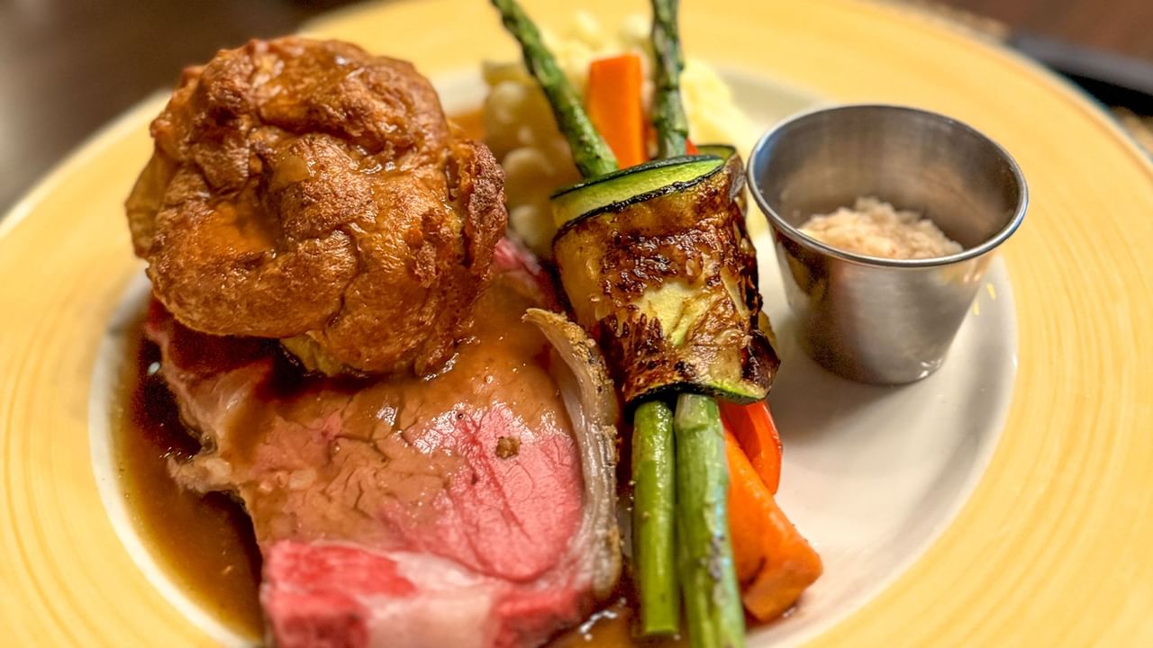 Plate of beef, vegetables, and a cup of seasoning.