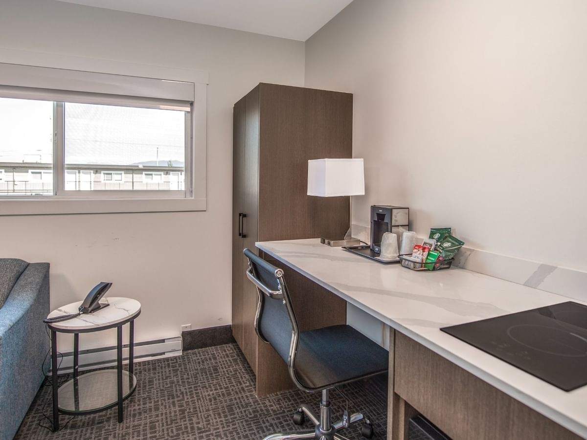 Modern hotel room with couch, desk with coffee maker, and window.