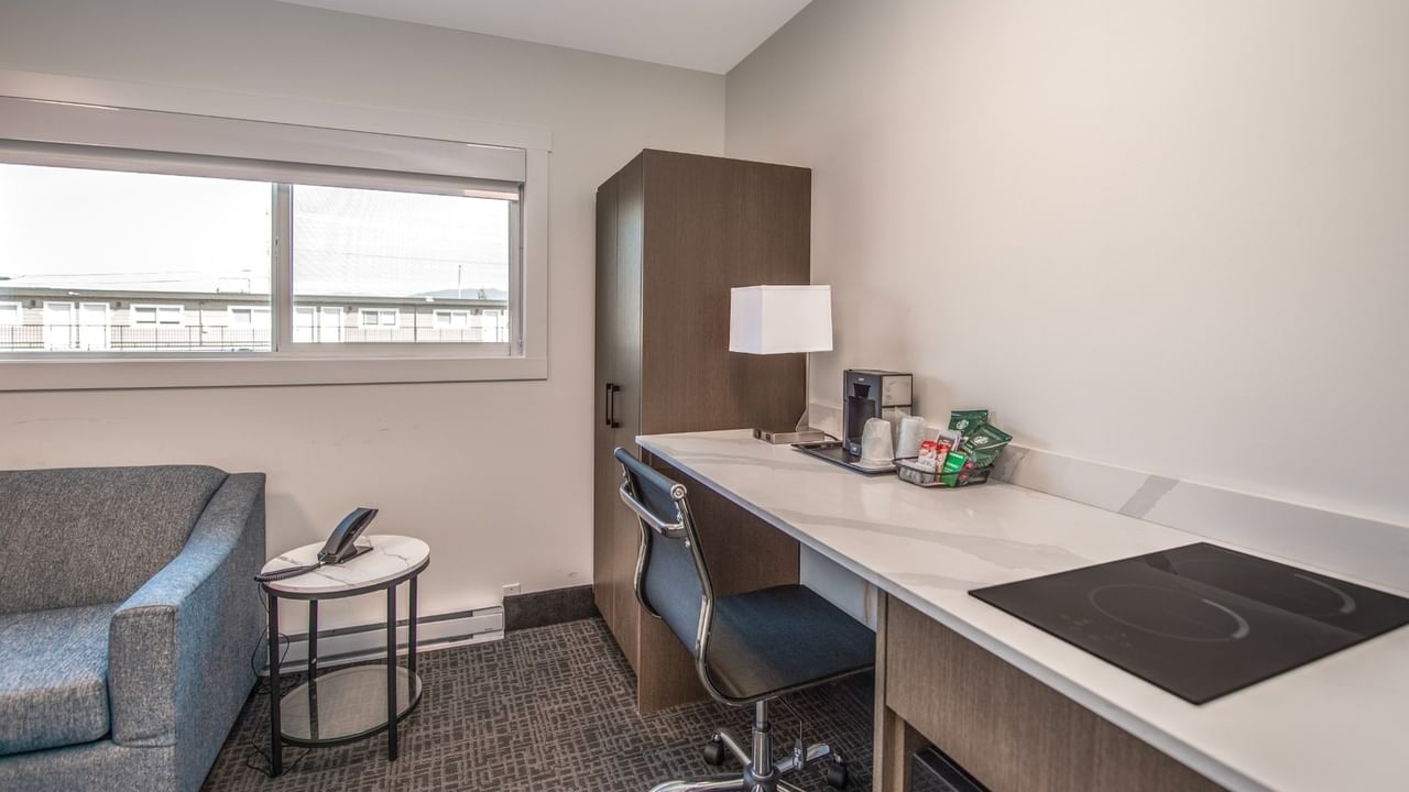 Modern hotel room with couch, desk with coffee maker, and window.