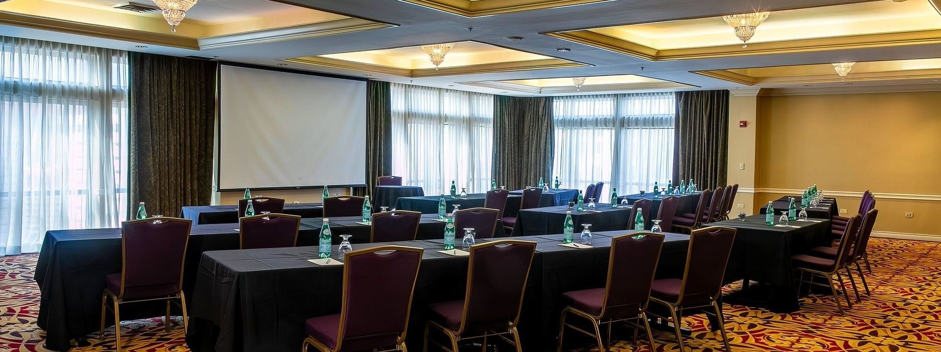 Black tables with purple chairs by a projector screen under crystal chandeliers in Millennium at Warwick Denver