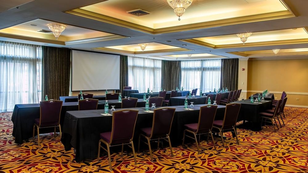 Black tables with purple chairs by a projector screen under crystal chandeliers in Millennium at Warwick Denver